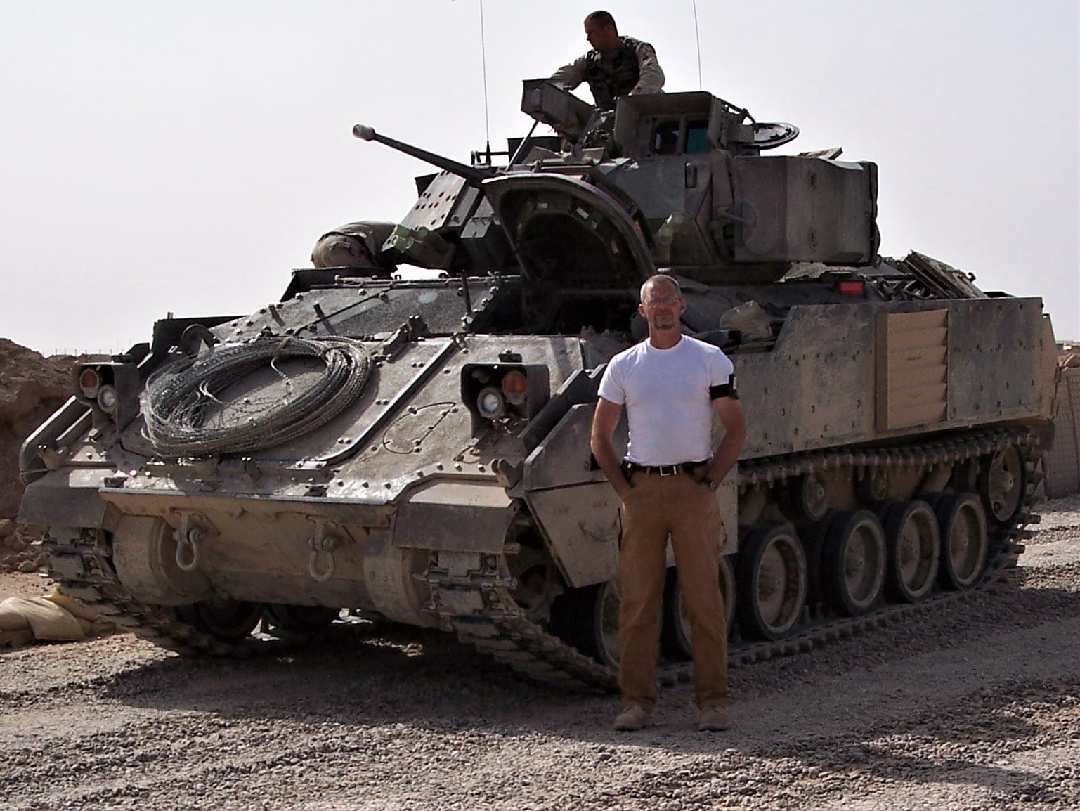 Paul Barnard stands in front of a tank at a military base.